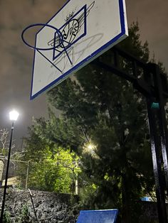 a basketball hoop with graffiti on it in front of some trees and street lights at night