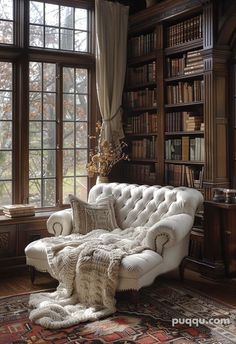 a white couch sitting in front of a window next to a book shelf filled with books