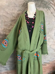 41023 Evil Eye Kimono Robe. How fun are these!!! We have more colors and prints coming soon. This olive-hued, handmade kimono-style robe is crafted from 100% organic cotton, and emblazoned with an all-seeing evil eye motif. With its gender-neutral design, it's a versatile, protective cover-up for the beach, the spa, festivals, or any time you want to bring a casual look to the next level. It's believed that the evil eye will keep wearers safe from negative energy and carry luck in other areas of Oversized Cotton Bohemian Kimono, Green Cotton Kimono For Spring, Spring Green Cotton Kimono, Bohemian Cotton Kimono For Fall, Casual Green Cotton Kimono, Oversized Cotton Kimono For Spring, Cotton Festival Kimono One Size, Green Wrap Kimono For Loungewear, One Size Cotton Festival Kimono