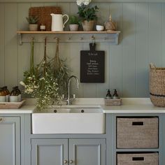 a kitchen with gray cabinets and white counter tops is pictured in this image, there are baskets on the shelf above the sink