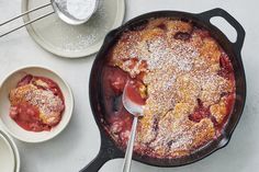 a skillet filled with fruit covered in powdered sugar next to two bowls and spoons