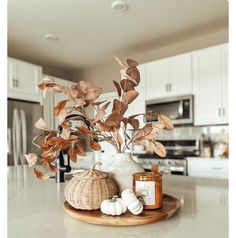 a white vase filled with lots of leaves on top of a wooden tray next to a bottle