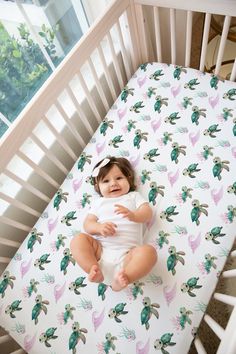 a baby sitting in a crib with a sheet on it's back and smiling at the camera