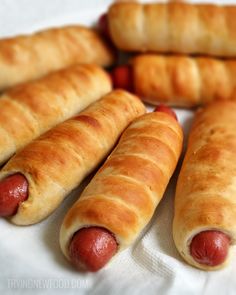 four hotdogs are lined up in a circle on a white tablecloth with croissants next to them