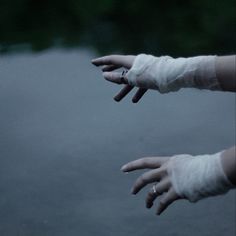 two hands with bandages on them reaching out to each other in front of a body of water