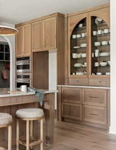 a large kitchen with wooden cabinets and stools next to an island counter top in front of two ovens