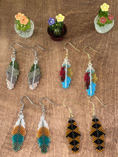 six pairs of beaded earrings sitting on top of a wooden table next to potted plants