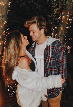 a man and woman standing next to each other in front of trees with lights on them