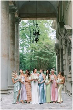 a group of women standing next to each other in front of a stone building holding bouquets