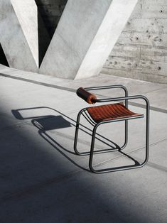 a chair sitting on the ground in front of a concrete wall and cement structure with an orange tube sticking out of it's back end