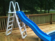 a blue slide sitting on top of a wooden deck next to a swimming pool in a backyard