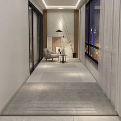 an empty hallway leading to a living room with large windows and a view of the city at night