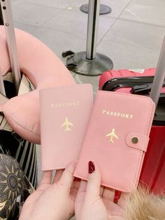 a pink passport case sitting on top of a pile of luggage next to a woman's hand