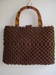 a brown crocheted purse hanging on a wall next to a white wall with a wooden handle