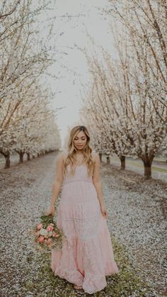 a woman standing in the middle of an apple orchard wearing a pink dress and holding a bouquet