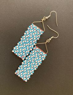 two blue and white beaded earrings sitting on top of a black surface with gold ear wires