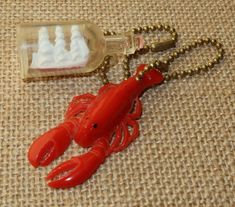 there is a red lobster keychain and a bottle on the ground with a white ship in it