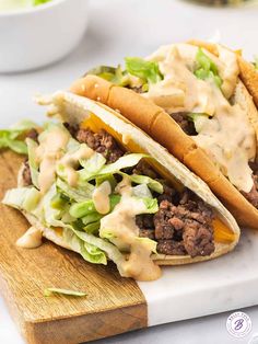 two tacos with lettuce, cheese and sauce on a wooden cutting board