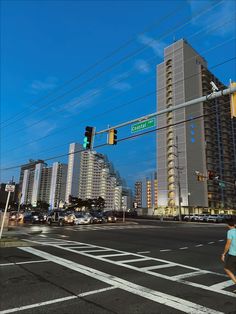 a woman crossing the street in front of tall buildings and traffic lights at an intersection