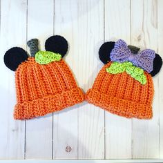 two crocheted hats with ears and bows on them, one is orange and the other is black