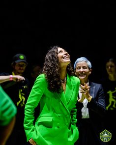 a woman in a green suit standing next to other people and clapping with her hands