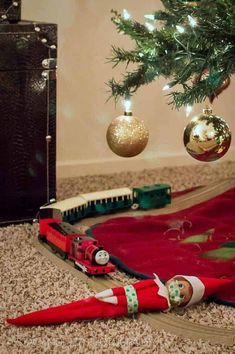 a christmas tree is next to an elf's train and other holiday decorations on the floor