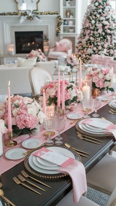 a dining room table set with pink and white flowers, candles and place settings in front of a christmas tree