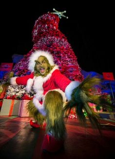 a man dressed as santa claus is dancing in front of a christmas tree at night