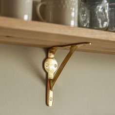 a shelf that has some cups and mugs on it with a gold hook in the middle