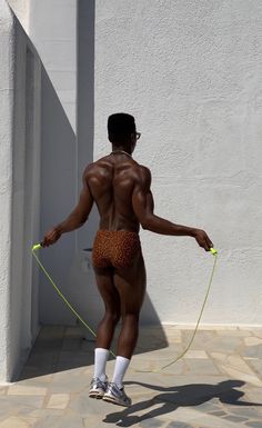 a man with no shirt on is holding a green rope and wearing white socks while standing in front of a building