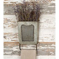 a metal planter with lavenders in it on a white wooden wall behind a towel holder