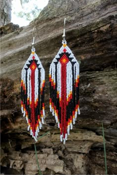 the beaded earrings are hanging from a tree branch in front of a rock wall