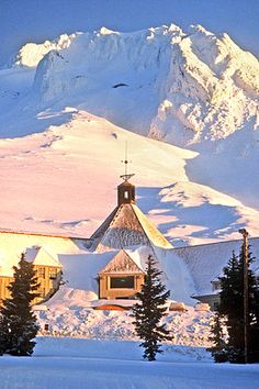 a church in the middle of a snowy mountain range with trees and snow covered mountains behind it