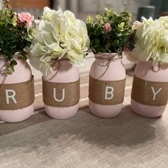 three pink mason jars with white flowers and the word ruby painted on them are sitting on a table