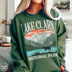 Show off your love of Alaska and one of our nation's most remote national parks with our Lake Clark National Park Sweatshirt! This comfy crewneck is all about embracing the great outdoors, featuring a custom vintage design that showcases the grandeur of the Alaskan Wilderness, the iconic Brown Bear, and the beautiful vistas across Lake Clark! The Gildan 18000 50/50 blend fabric has that comfy, lived-in feel, that's like a hug every time you put it on! Now you can take a bit of Lake Clark with yo National Park Sweatshirt, National Park Gifts, California Sweatshirt, National Park Shirt, Sequoia National Park, Great Smoky Mountains National Park, Beautiful Park, Smoky Mountain National Park, A Hug