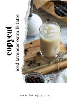 a glass filled with liquid sitting on top of a wooden cutting board next to nuts