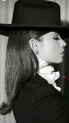 a woman wearing a black hat with white ruffles on her neck and long hair