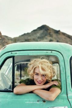 a woman sitting in the drivers seat of an old green truck with her arms crossed