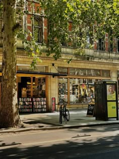 a bike parked on the side of a street next to a tree and book store