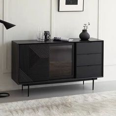 a black sideboard with two drawers and a lamp on the floor next to it