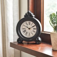 a black clock sitting on top of a wooden table next to a potted plant