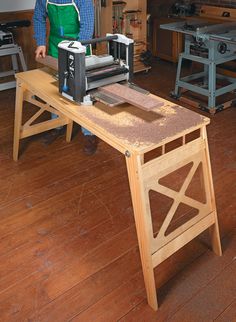 a man standing next to a table sawing on top of a piece of wood