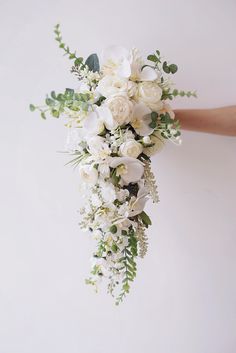 a bridal bouquet with white flowers and greenery is being held by someone's hand