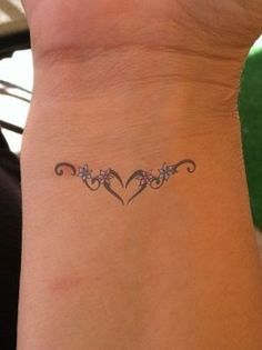 a woman's wrist tattoo with two hearts and flowers in the middle on her left arm