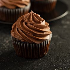 two chocolate cupcakes sitting on top of a black plate next to each other