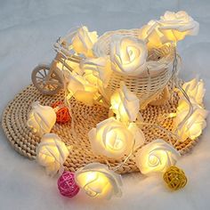 some white roses are sitting on a wicker basket with lights in it and one is lit up