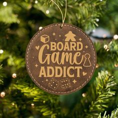 a christmas ornament that says board game addict hanging from a tree with lights in the background