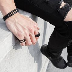 a man sitting on top of a cement bench wearing black bracelets and holding onto his hand