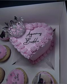 a pink heart shaped cake in a box with cupcakes and a crown on top