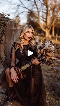 a woman in a black dress sitting on a rock holding a bunch of dried flowers